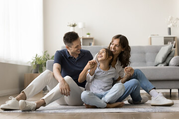 Happy young family sitting on warm floor in cozy living room, playing together with kid, spend time...