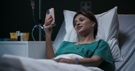 Young patient lies in a hospital room, an oxygen tube in her nose, chatting via video call.