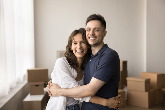 Portrait of laughing couple in love hugging, looking at camera resting, take break on relocation day, feel happy, enjoy first day at their own house or flat. Independence, life changes, tenancy, rent