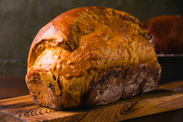 Sweet brioche bun on wooden cutting board, on a dark background. Delicious home baked goods