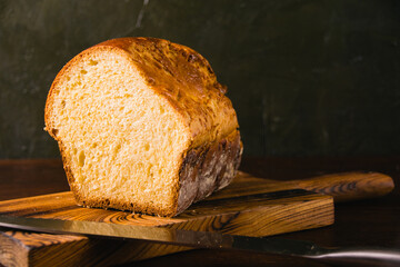 Sweet brioche bun cut on a wooden cutting board and bread knife. Delicious home baked goods