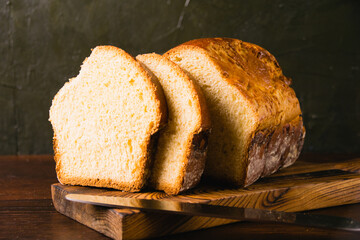 Sweet brioche loaf cut into slices on a wooden cutting board and a bread knife. Delicious homemade...