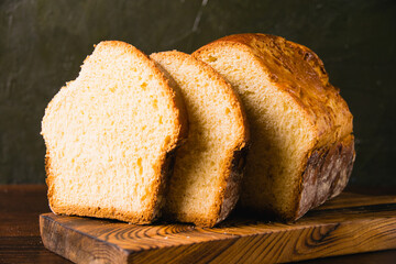 Delicious and sweet buttery bread cut into slices on a dark wooden cutting board. Delicious home baked goods