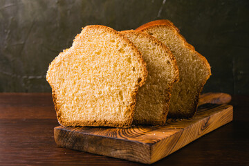 Delicious and sweet buttery bread cut into slices on a dark wooden cutting board. Delicious home baked goods