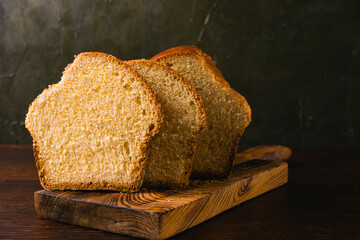 Delicious and sweet buttery bread cut into slices on a dark wooden cutting board. Delicious home baked goods