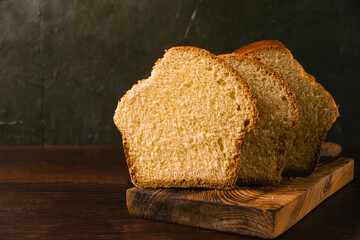 Delicious and sweet buttery bread cut into slices on a dark wooden cutting board. Delicious home...