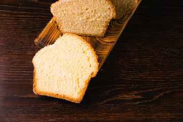 Delicious and sweet buttery bread cut into slices on a dark wooden cutting board. Delicious home baked goods