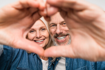 Beautiful middle age couple wearing denim shirt standing over isolated white background smiling in love showing doing heart symbol shape with hands studio shot. Romantic Valentine's Day love concept.