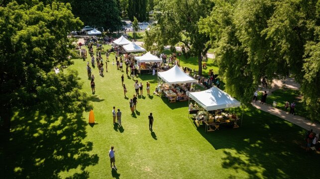 Sunny outdoor market with white tents and diverse crowd in lush green park