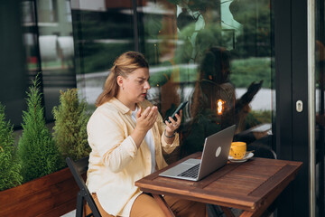Upset sad, skeptical, serious woman holding smartphone gadget for communicate outdoors. 30s woman using phone in public cafe, negative emotion. Urban lifestyle concept.