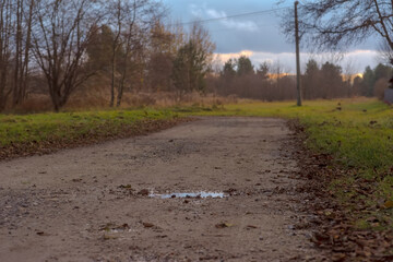 Droga gruntowa (utwardzona żwirem) biegnąca przez łąki po zachodzie słońca. Zakręt na drodze gruntowej po zachodzie słońca w pogodny jesienny wieczór.