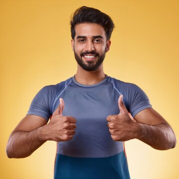 Jeune Homme Souriant en T-Shirt Bleu avec Deux Pouces Lev&eacute;s sur un Fond Jaune