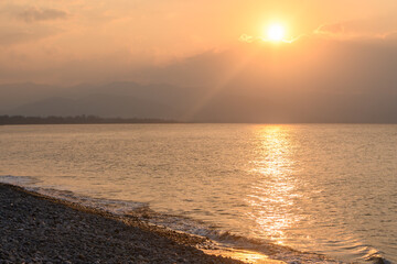 Naklejka premium Sunset paints the sky with warm hues over a tranquil shoreline at dusk