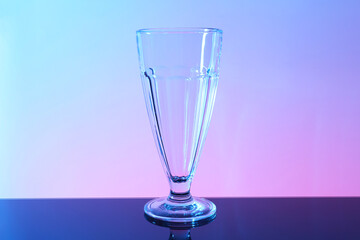 One empty glass on table against color background