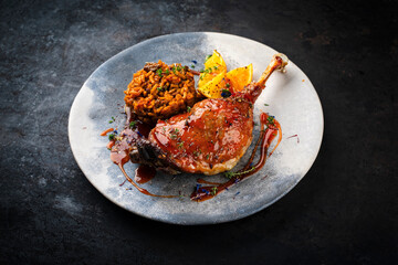 Traditional barbecue gourmet duck haunch with mushroom risotto and orange slices served with spicy chili sauce as close-up on a design plate