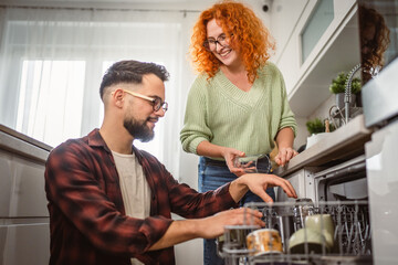 girlfriend help boyfriend to put dishes in dishwasher in kitchen