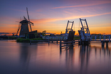 Obraz premium Eine Windmühle mit Brücke im UNESCO Weltkulturerbe Kinderdijk nahe Rotterdam bei Sonnenuntergang, Niederlande