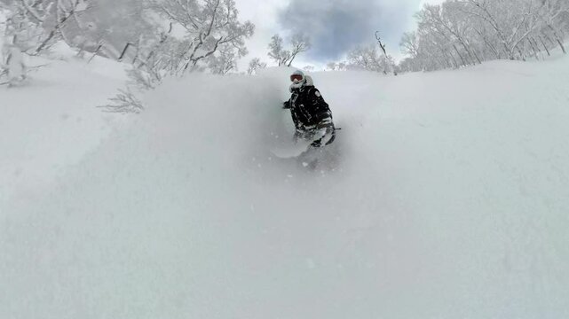 SELFIE: Snowboarder sprays clouds of fresh snow while riding off the ski slope. White frosted trees, deep powder and smiling face capture the thrill of backcountry snowboarding in Japanese mountains.