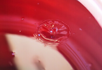 Close-Up View of Water Droplet Impact on Red Liquid Surface