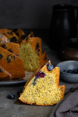 Closeup of Orange Blueberry Bundt Cake slice with poppy seed and icing. Homemade bakery. Fresh fruits on background. Dark grey table, vertical image.