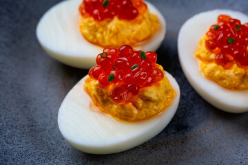 Close up of spiced deviled egg with salmon caviar on a blue plate.
