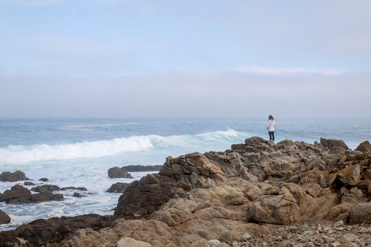 Female standing on rocks watching waves