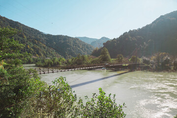 picturesque suspension bridge spans serene river surrounded by lush green mountains in mountainous Adjara, Georgia. vibrant landscape creates peaceful, natural setting. Concept of nature exploration