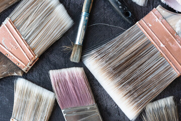 Top Down Close-Up of Assorted Paintbrushes with Worn Bristles and Handles on a Textured Dark Surface – Artistic Tools for Painting, DIY Projects, Home Renovation, or Creative Craft Background
