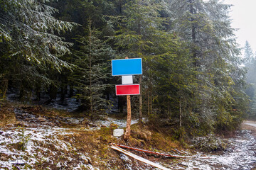 wooden information board  with Blue and Red Signs in Snowy Evergreen Forest