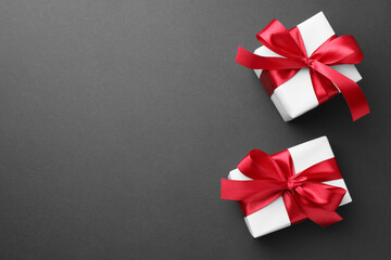Gift boxes with red bows on black background, top view. Space for text