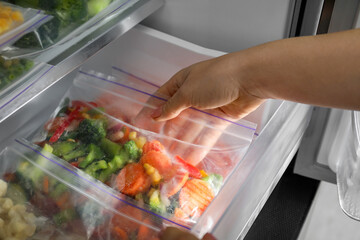 Woman taking plastic bag with mix of frozen vegetables from refrigerator, closeup