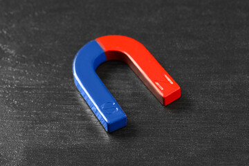 One horseshoe magnet on black wooden table, closeup