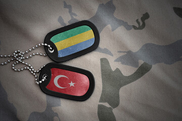 vintage army blank, dog tag with flag of gabon and turkey on the khaki texture background. military...