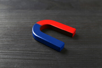 One horseshoe magnet on black wooden table, closeup