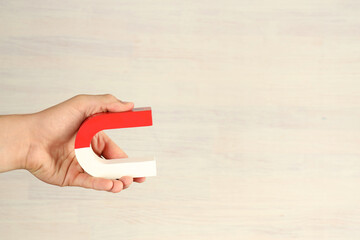 Man holding horseshoe magnet against white wooden background, closeup. Space for text