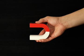Man holding horseshoe magnet on dark background, closeup