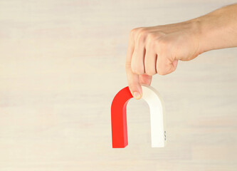 Man holding horseshoe magnet against light background, closeup. Space for text