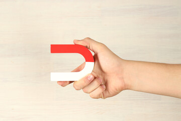 Man holding horseshoe magnet against white wooden background, closeup