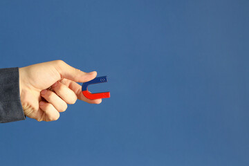 Man holding horseshoe magnet on blue background, closeup. Space for text