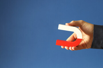 Man holding horseshoe magnet on blue background, closeup. Space for text