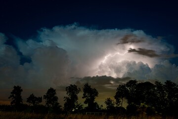 A dramatic nighttime scene with a stormy sky lit by a brilliant bolt of lightning. Dark clouds billow across the horizon, casting shadows on the landscape, creating a breathtaking atmosphere.