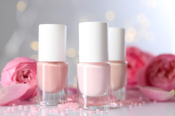 Nail polishes in bottles, beads and beautiful flowers on white table, closeup