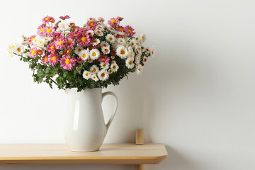 Vase with beautiful flowers on wooden shelf near white wall, space for text