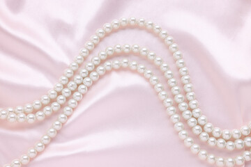 Elegant pearl necklace on pink fabric, top view