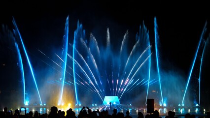 Impressive performance of dancing fountain with blue water jets and bright lights at night. The illuminated water jets create a mesmerizing spectacle against the dark sky.