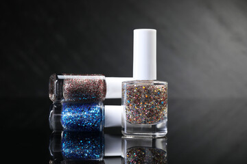 Set of glitter nail polishes in bottles on black mirror surface, closeup