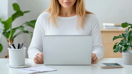 Fototapeta premium Young woman working on a laptop at a bright and cozy home office with plants and stationery around her