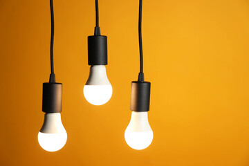 Light bulbs hanging on cords against orange background, space for text