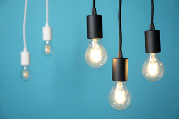 Light bulbs hanging on cords against blue background, selective focus