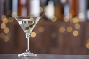 Martini cocktail with olives in glass on wooden table against blurred background. Bokeh effect